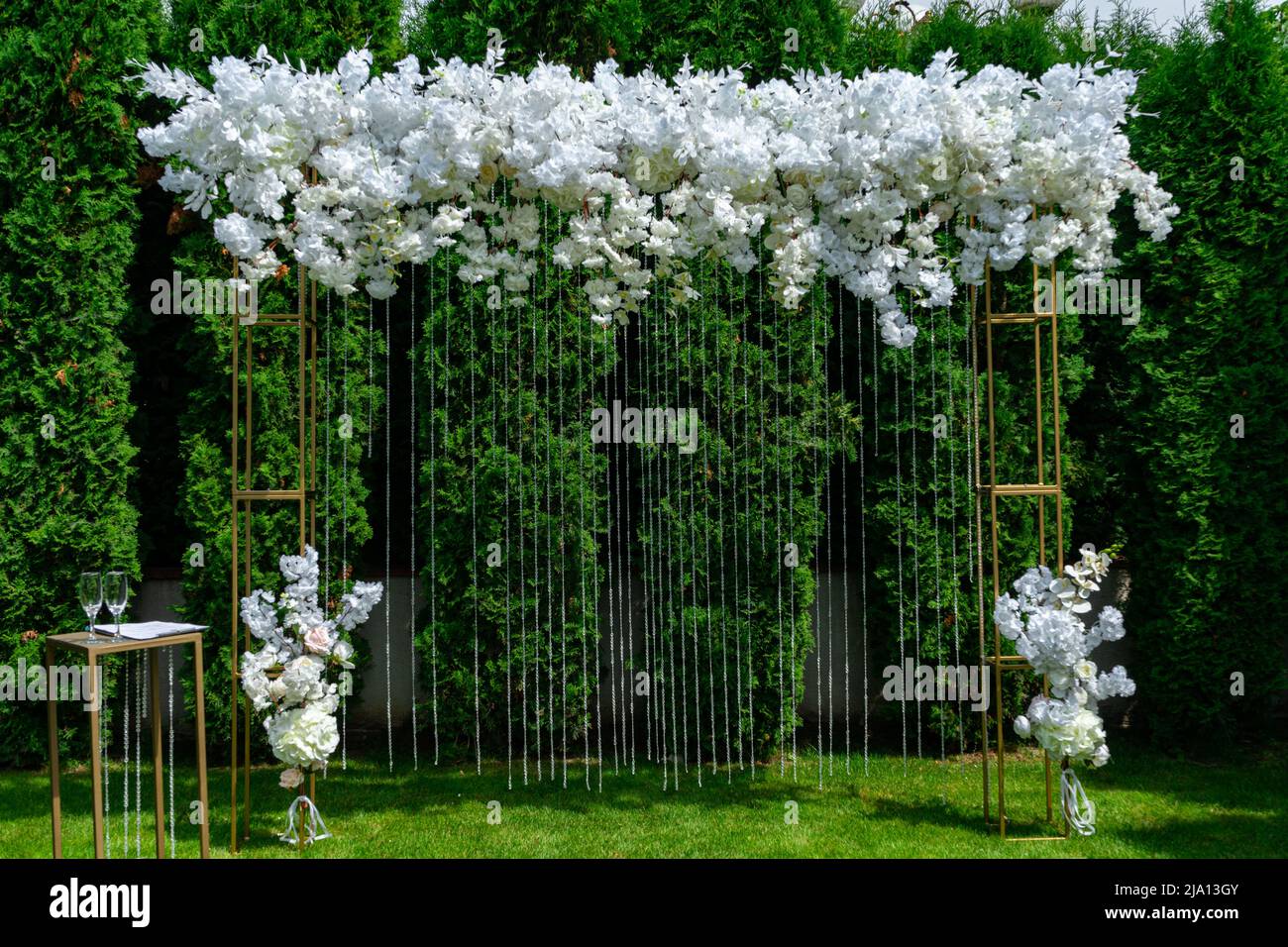 Arco di nozze bianco su uno sfondo di tuja sempreverde. Cerimonia di nozze estiva nel parco Foto Stock