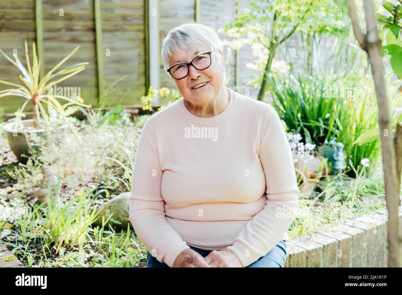 Ritratto di sorridente anziano, matura nonna in pensione in occhiali. Donna anziana felice sorridendo seduto nel suo giardino verde e godendo la pensione Foto Stock