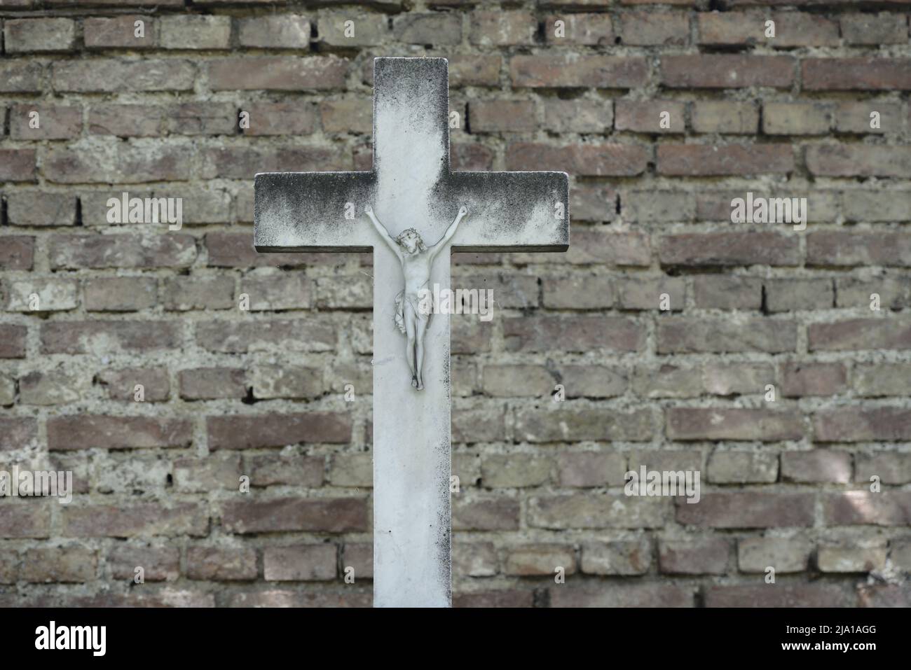 Vienna, Austria. Il cimitero centrale di Vienna. Croce di pietra di fronte ad un muro di mattoni Foto Stock