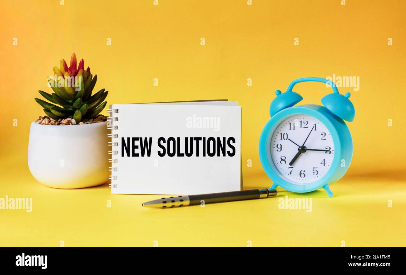 Concetto aziendale. Sul taccuino c'è un'iscrizione - NUOVA SOLUZIONE su sfondo giallo con un orologio e un fiore. Miniature di persone Foto Stock Concetto aziendale. Sul taccuino c'è un'iscrizione - NUOVA SOLUZIONE su sfondo giallo con un orologio e un fiore. Miniature di persone Foto Stock
