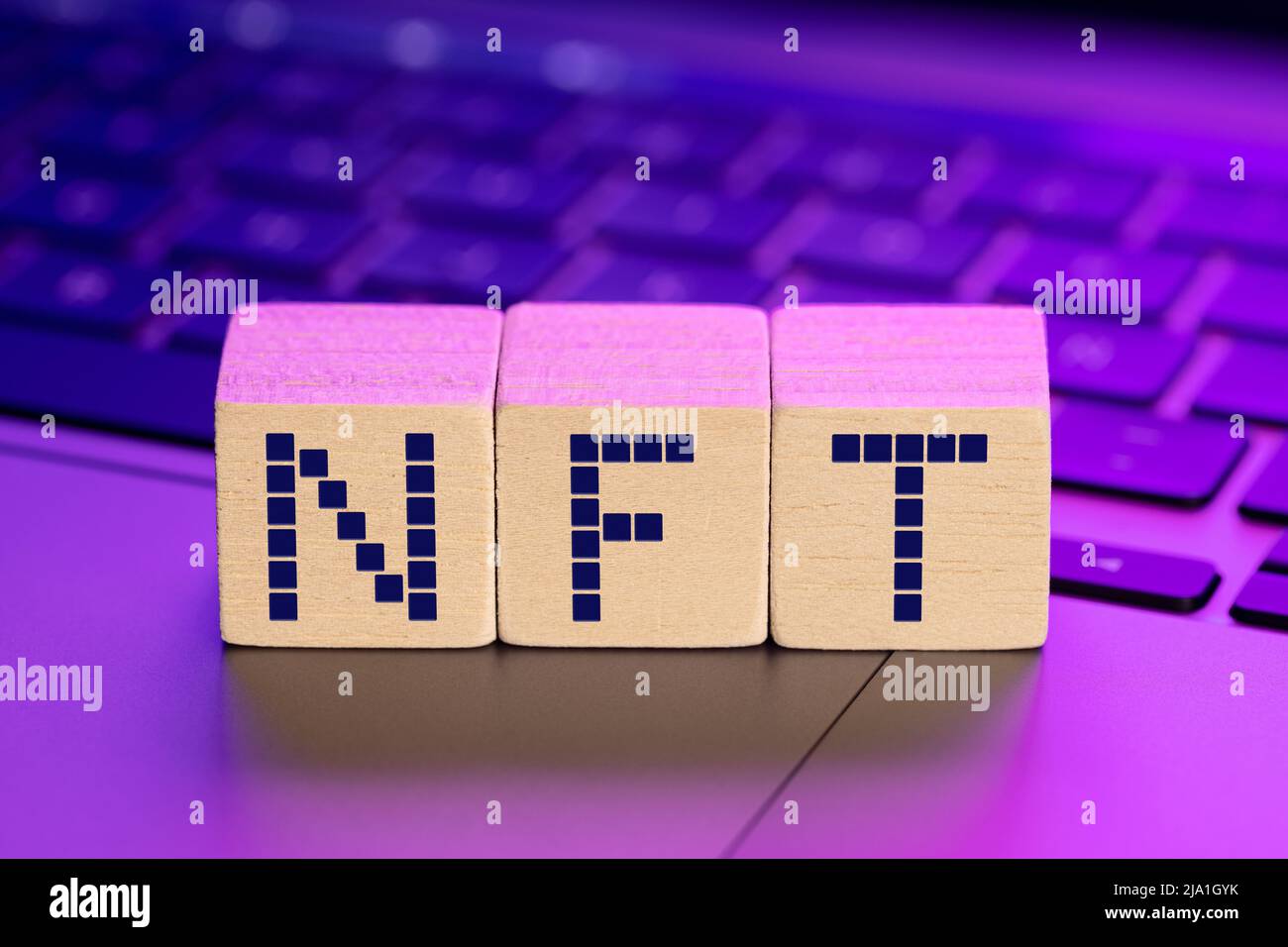 NFT parola su blocchi di legno su laptop con luci colorate. Concetto di token non fungibile Foto Stock