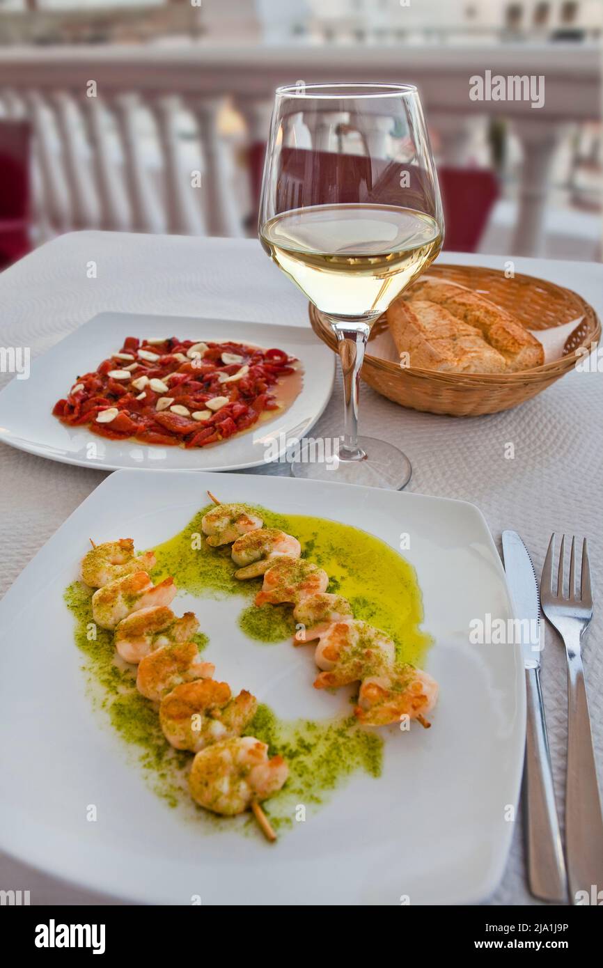 Un delizioso pasto all'aperto a base di spiedini di gamberi alla griglia, insalata di peperoni arrosto e un bicchiere di vino a Salobrena, Spagna Foto Stock