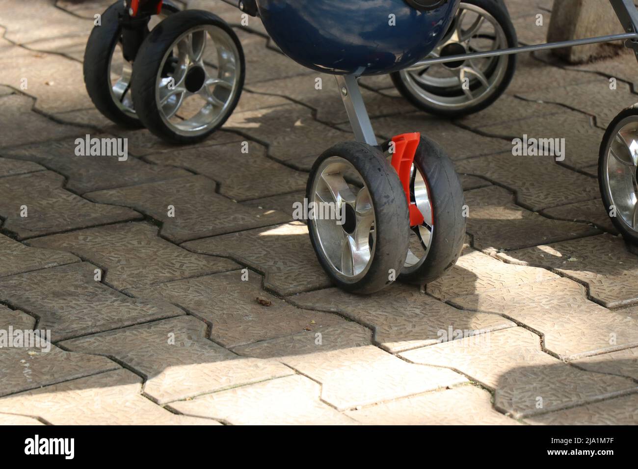 Ruote con passeggini con serratura di sicurezza che poggiano su piastrelle di interblocco in luce diurna Foto Stock