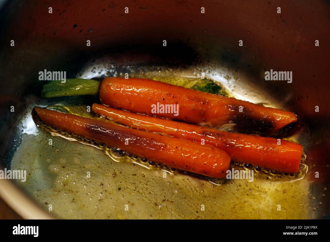 burro carote glassate in una padella metallica con sale e pepe Foto Stock