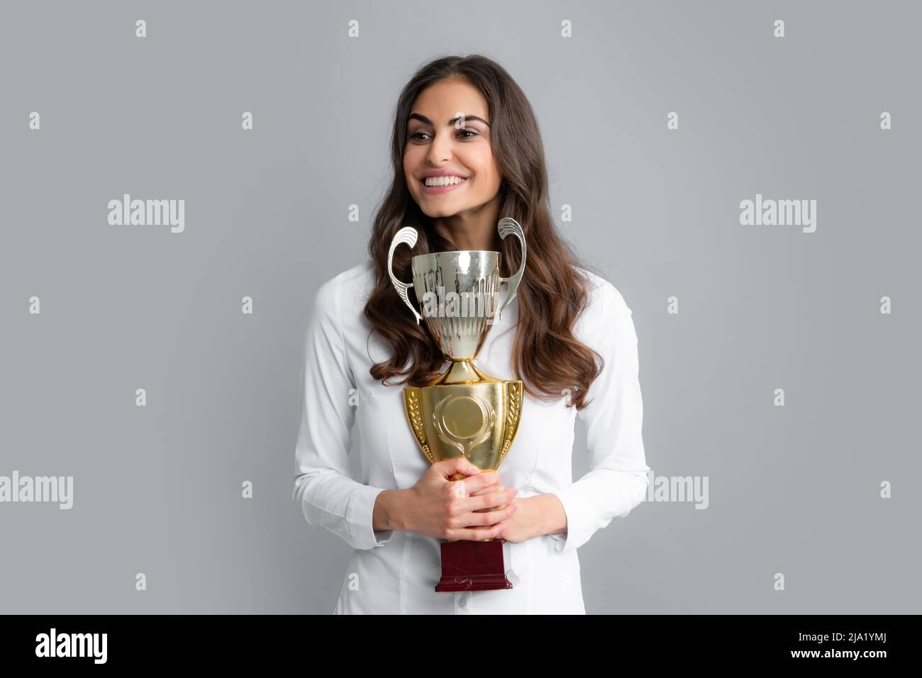 Donna d'affari allegra che tiene il trofeo in piedi in posa su sfondo grigio. Il dipendente di successo detiene la coppa del vincitore. Cerimonia di premiazione per il vincitore. Ottimo Foto Stock