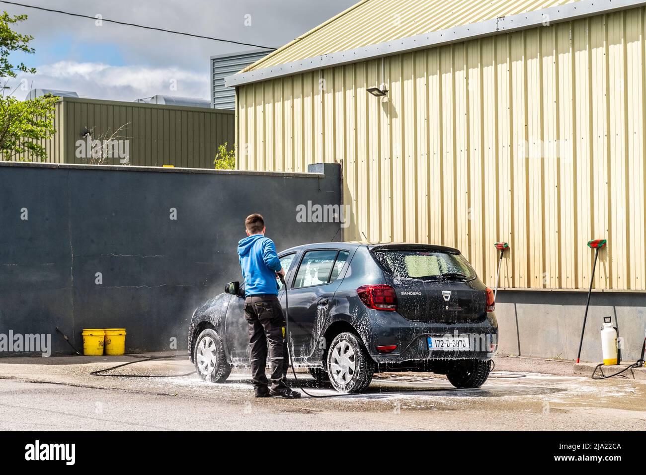 Uomo lavaggio auto in un lavaggio auto commerciale utilizzando un tubo ad alta pressione acqua in Irlanda. Foto Stock