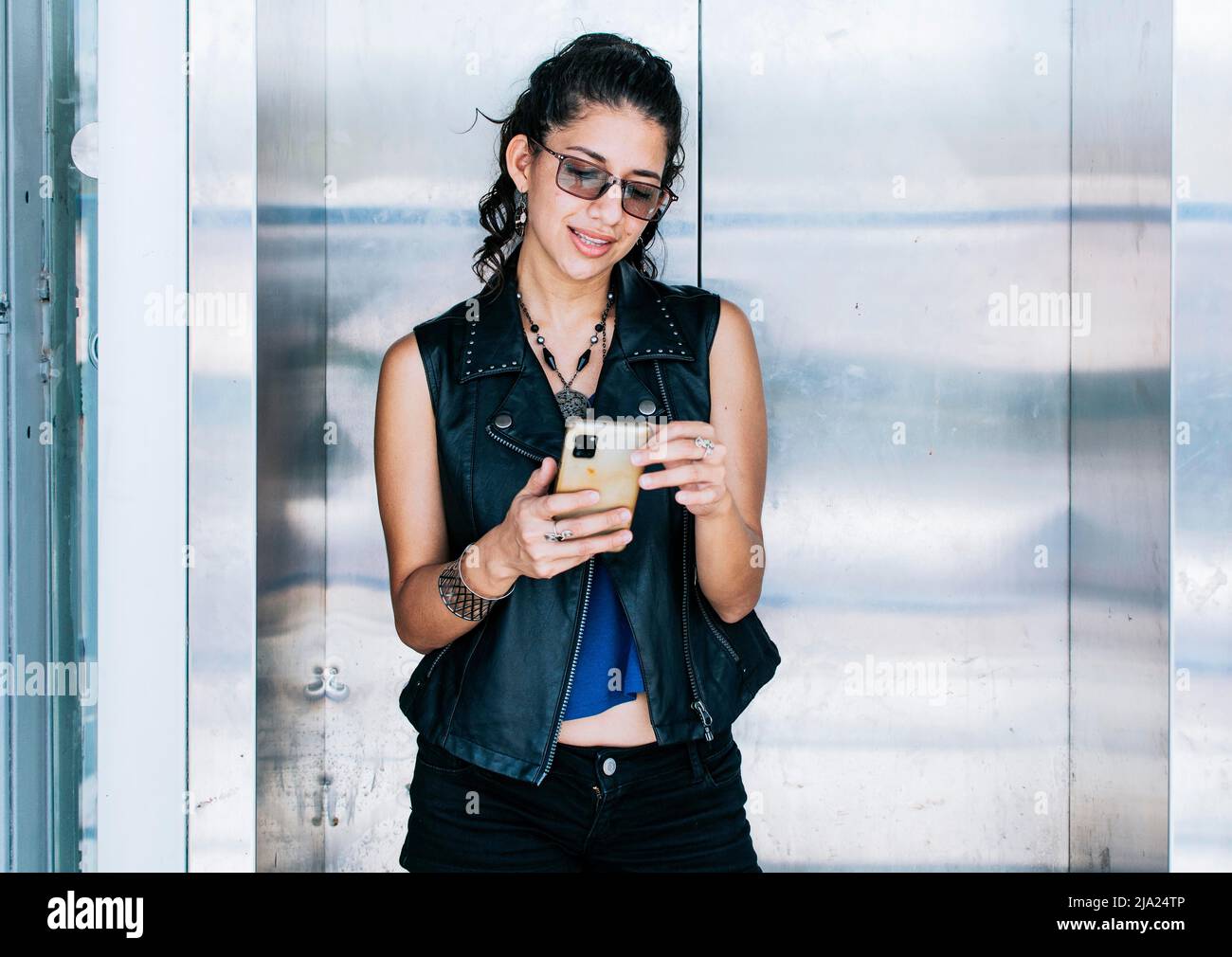 Ragazza attraente usando il suo telefono delle cellule alla porta dell'ascensore, Una persona che texting nell'ascensore, primo piano della ragazza urbana che controlla il suo telefono delle cellule Foto Stock