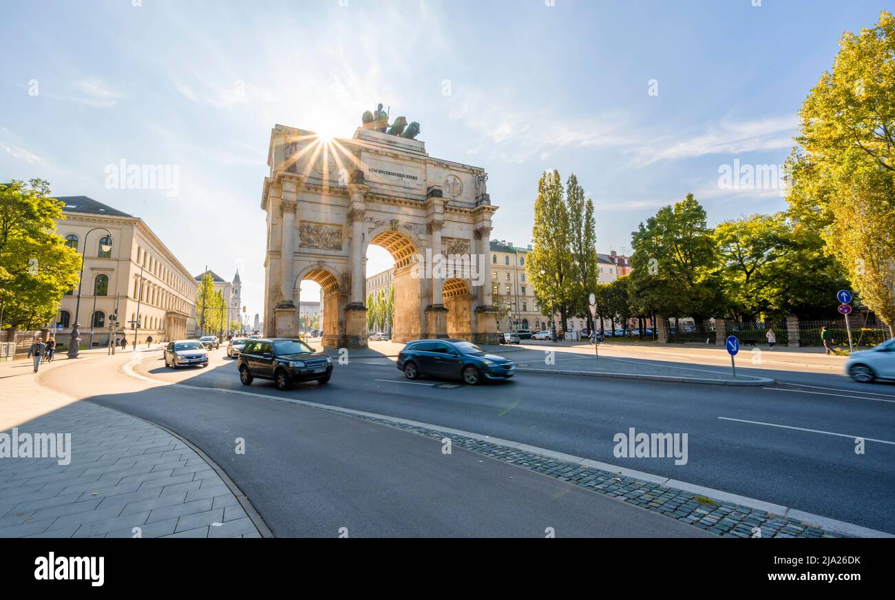 Sun Star, Siegestor, Cars guidare lungo Leopoldstrasse, architettura neoclassica, Baviera, Monaco, Baviera, Germania Foto Stock