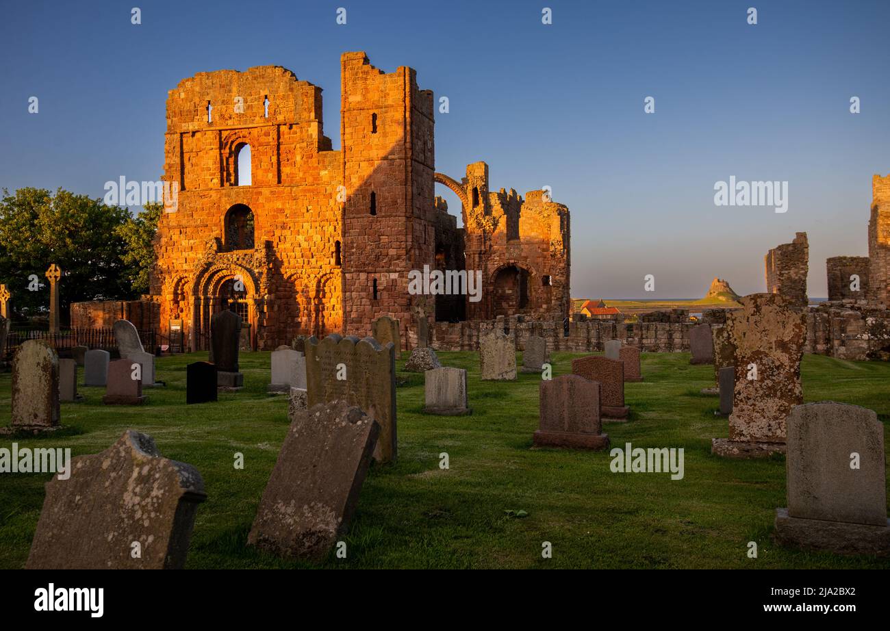 Gli ultimi raggi del sole serale illuminano le rovine del Priorato di Lindisfarne con il Castello in lontananza, Holy Island, Northumberland, Inghilterra, Regno Unito Foto Stock