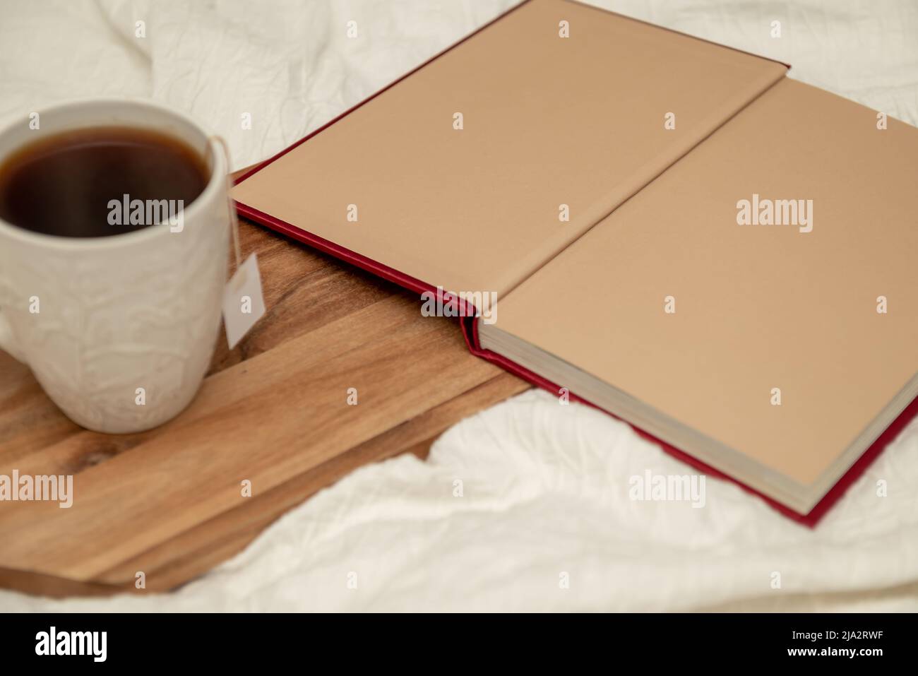 Libro aperto e tazza di tè a letto con biancheria bianca. Foto Stock