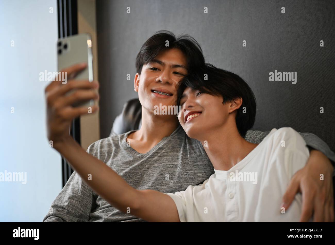 Coppia gay teen asiatica prendendo un selfie insieme in salotto, la mano del partner è intorno al suo amante, mostrando un po 'di affetto LGBT. Concetto LGBT Foto Stock