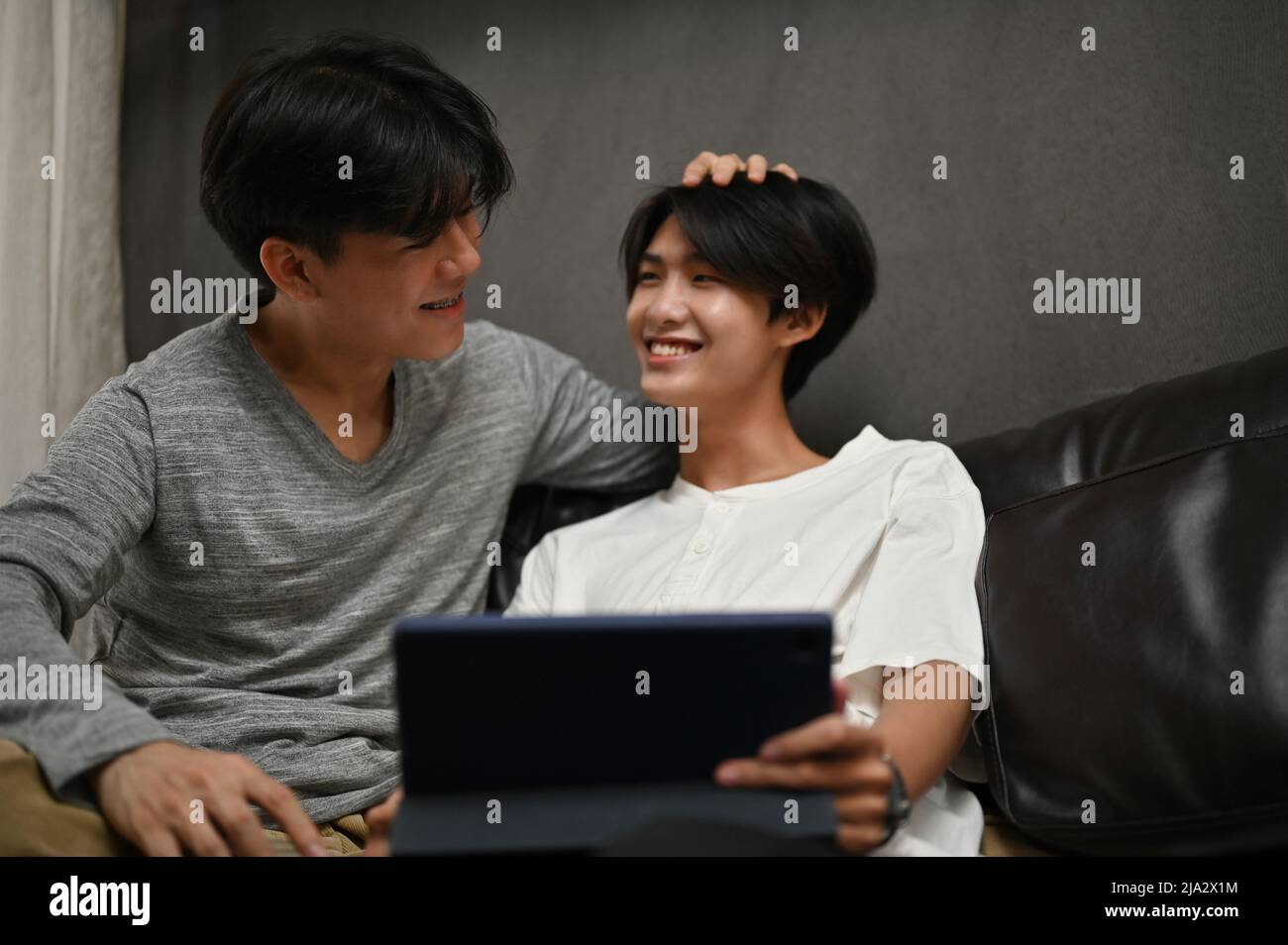 Due giovani coppie gay asiatiche si rilassano nel soggiorno e si godono guardare film su tablet digitale. LGBT amore affetto. Foto Stock