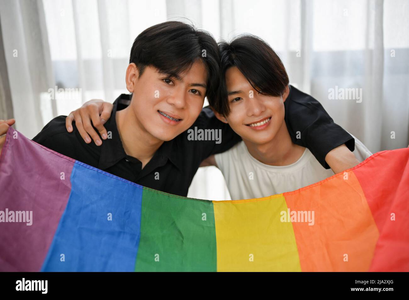 LGBT amore coppia concetto, bello asiatico adolescenti gay uomini coppia braccia intorno a vicenda e tenendo una bandiera arcobaleno LGBT. Foto Stock
