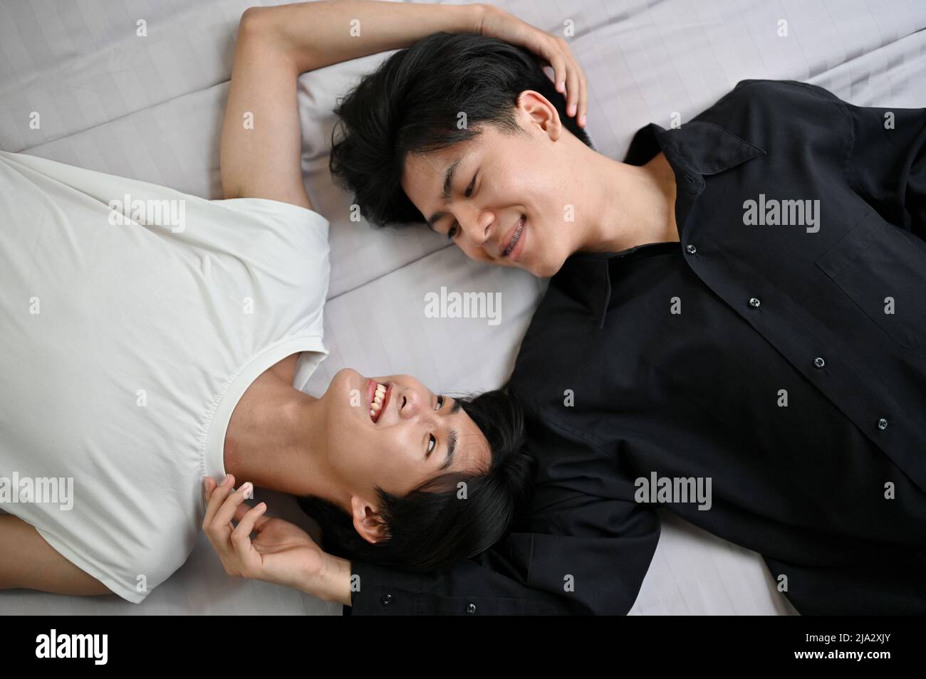 Top shot di una coppia di giovani gay asiatici amorevoli sdraiati a letto insieme, mani l'una intorno all'altra, condividendo momenti speciali romantici. Concetto di coppia LGBT Foto Stock