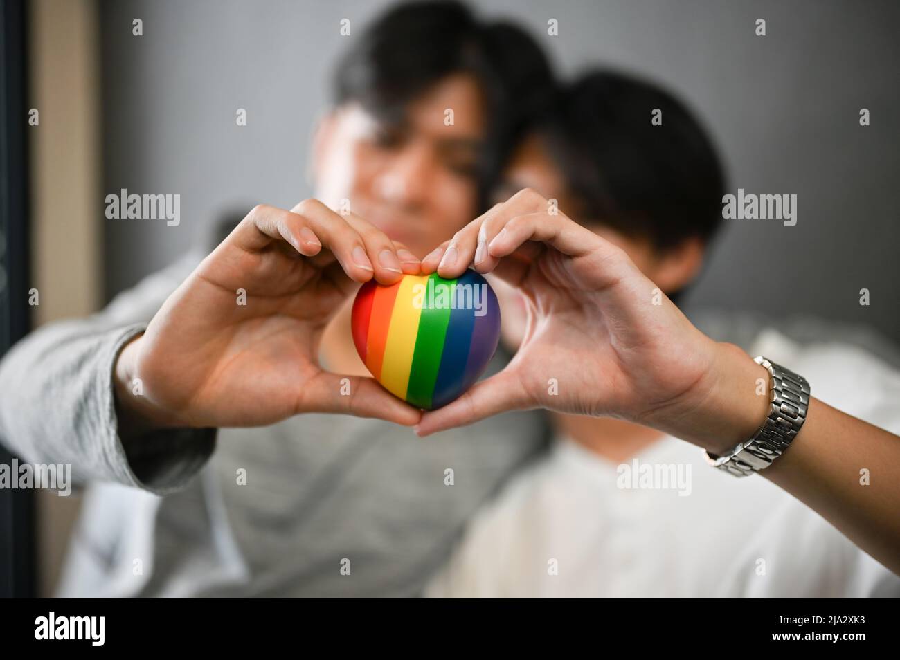 Primo piano immagine, due gay asiatici coppia di uomini tenendo un cuore arcobaleno e facendo una forma di cuore con le mani. Simbolo dell'amore LGBT. Foto Stock