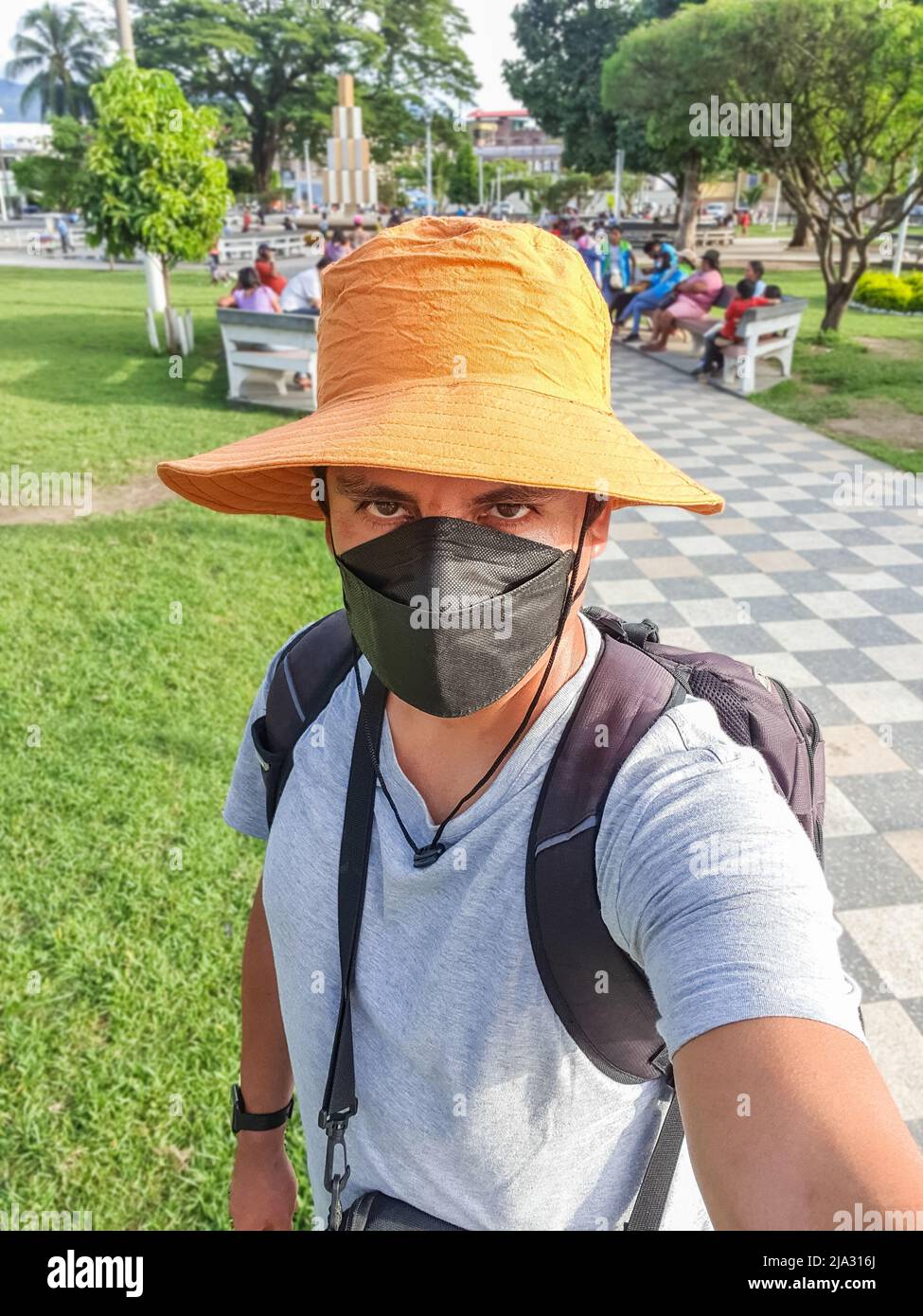 Ritratto di un turista con una maschera medica, zaino, e macchina fotografica prendendo un selfie con un telefono cellulare Foto Stock