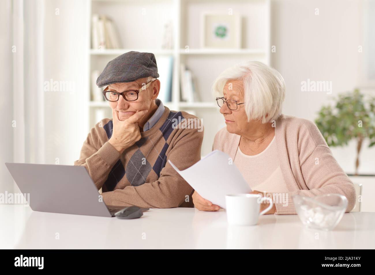 Uomo anziano che pensa e donna anziana che tiene un documento e guarda un computer portatile Foto Stock