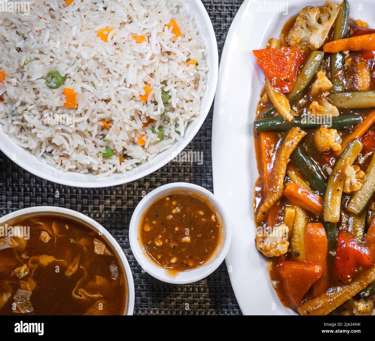 Vista dall'alto di riso fritto vegetale, verdure esotiche saltate, zuppa calda e acida e salsa di pepe su sfondo di un tappeto da tavolo. Foto Stock