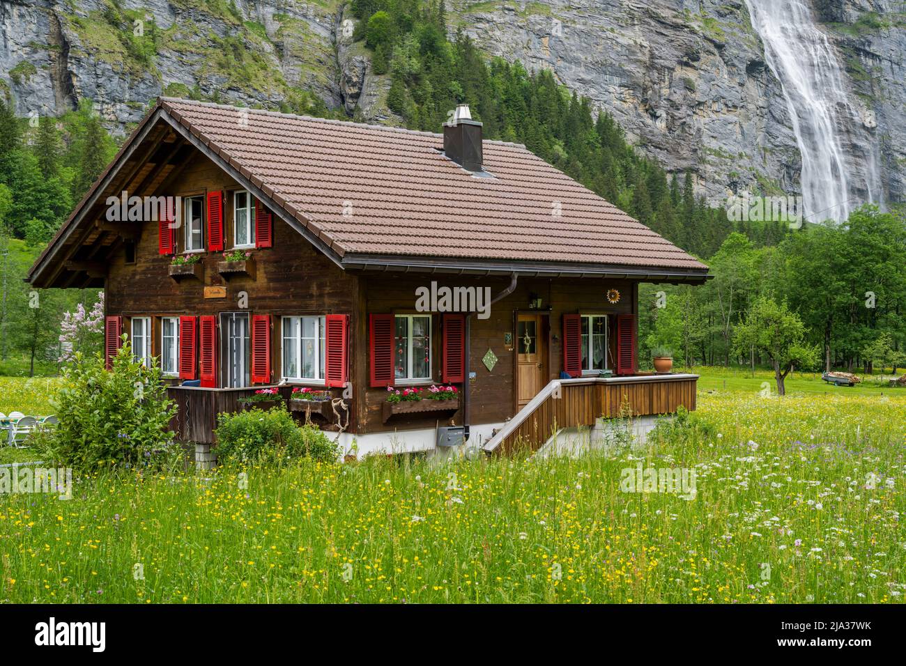 Tipica casa di montagna svizzera con cascata alle spalle, Lauterbrunnen, Cantone di Berna, Svizzera Foto Stock