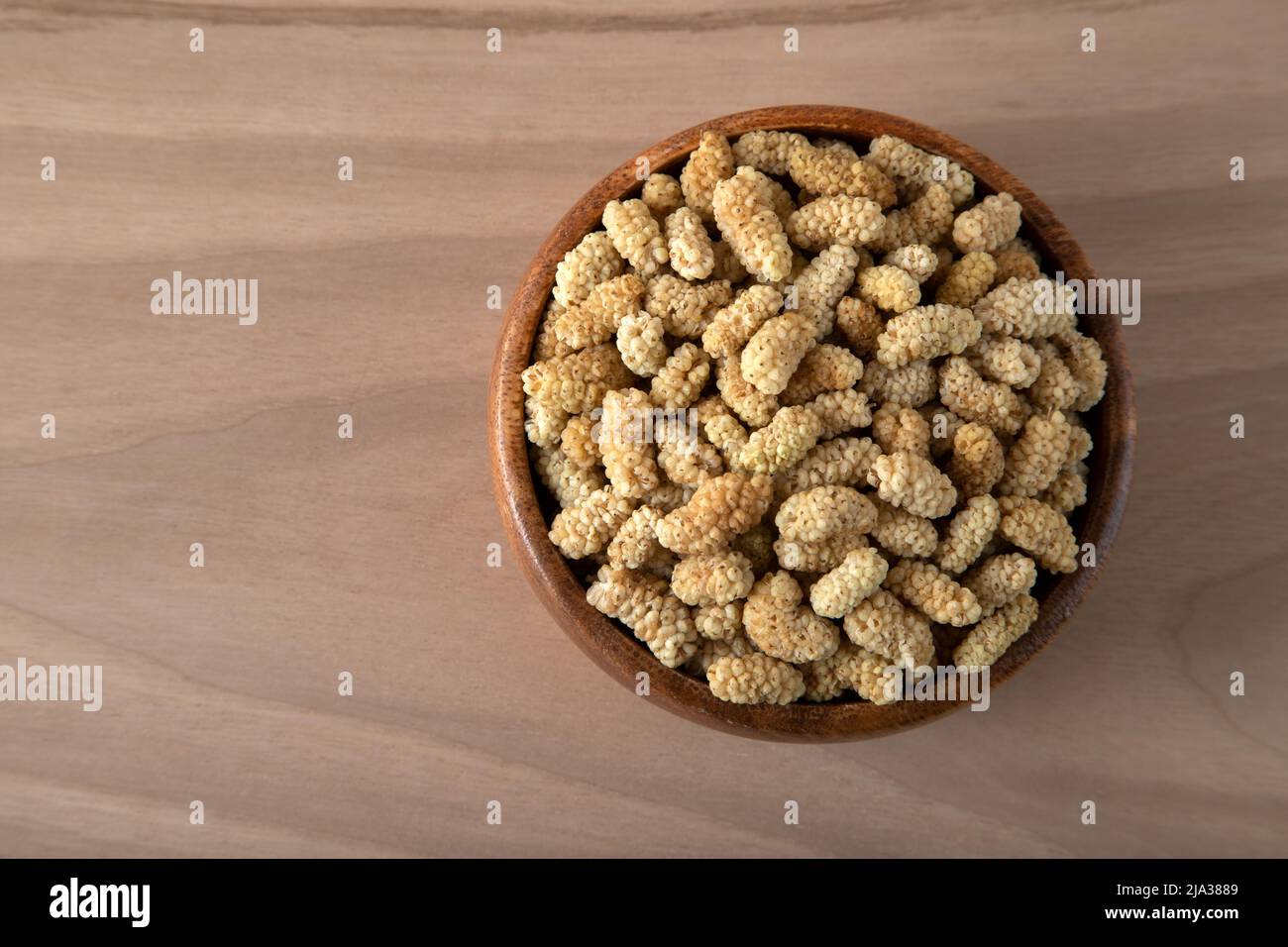 Ciotola piena di gelso secco su sfondo di legno Foto Stock