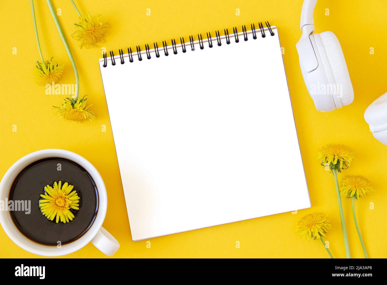 Layout minimalista estivo realizzato con notebook bianco, cuffie e tazza di caffè su sfondo giallo. Modello in stile piatto. Vista dall'alto. Foto Stock