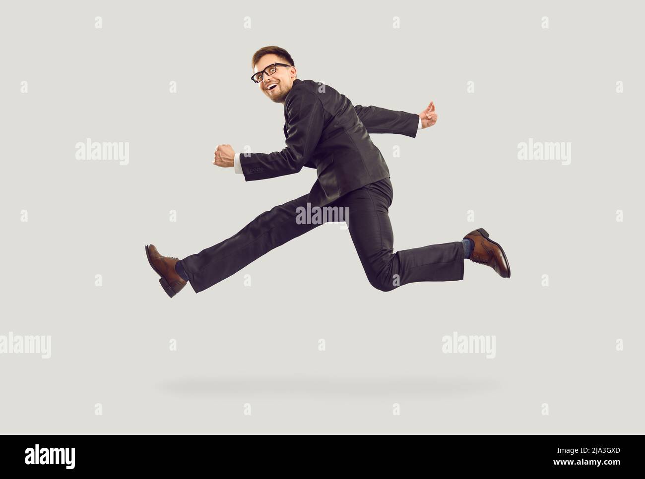 Folle eccitato giovane uomo d'affari in abito nero corsa e salto isolato su sfondo grigio. Foto Stock