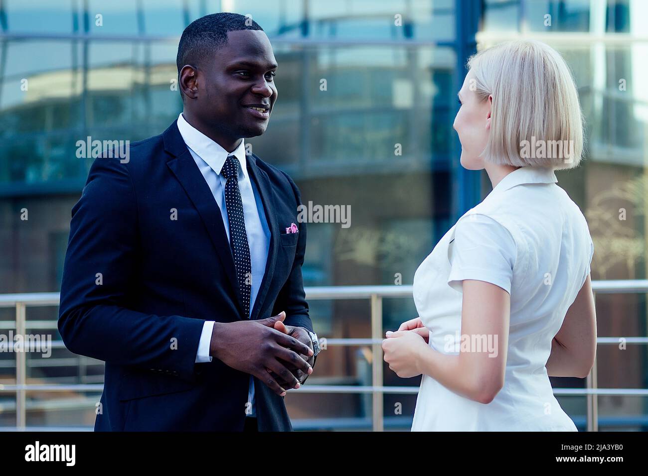 Bell'uomo d'affari afroamericano in un abito nero elegante che parla con attraente donna bionda donna di affari sulla strada sfondo ufficio Foto Stock