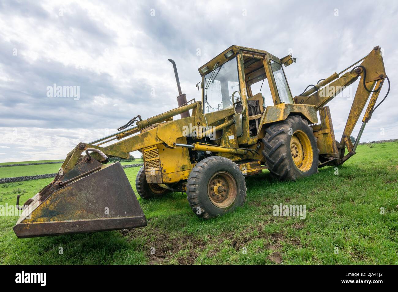 Un vecchio caricatore retroescavatore Ford si trova al sole di un campo vicino ad Appleby, Yorkshire. Avvistato mentre si fa la passeggiata Dales High Way. Foto Stock