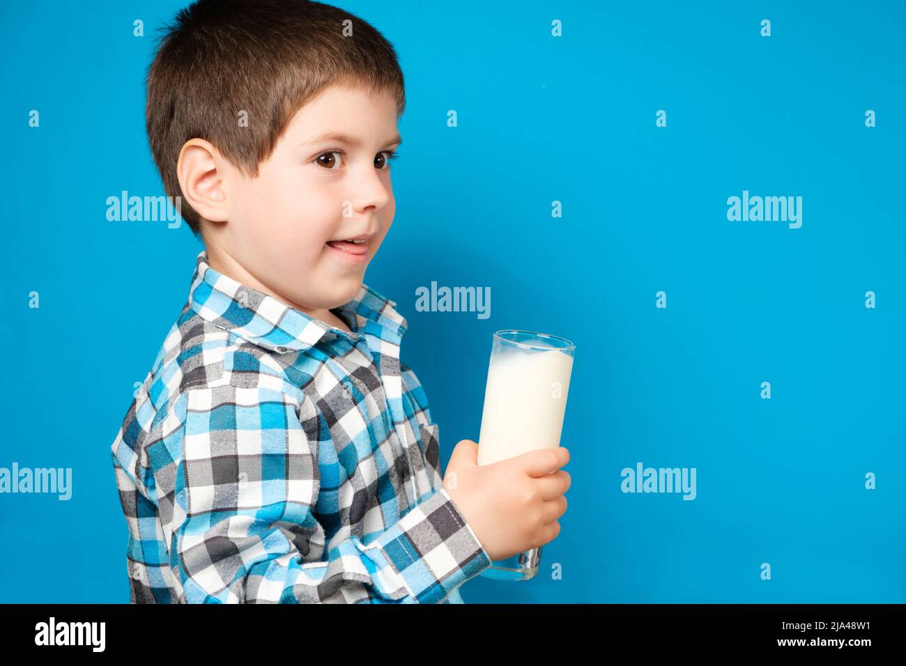 Un ragazzo di 4 anni sorride e tiene un bicchiere di latte su sfondo blu, un luogo per il testo Foto Stock