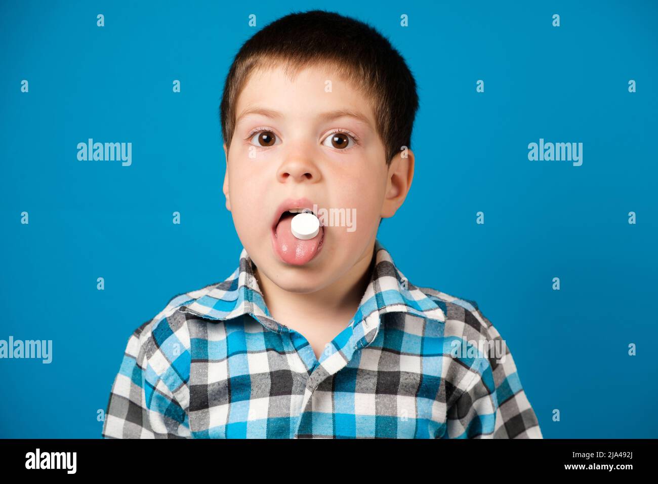 Un ragazzo bello preschool mangia la vitamina C o altre medicine o integratori alimentari su sfondo blu. Foto Stock