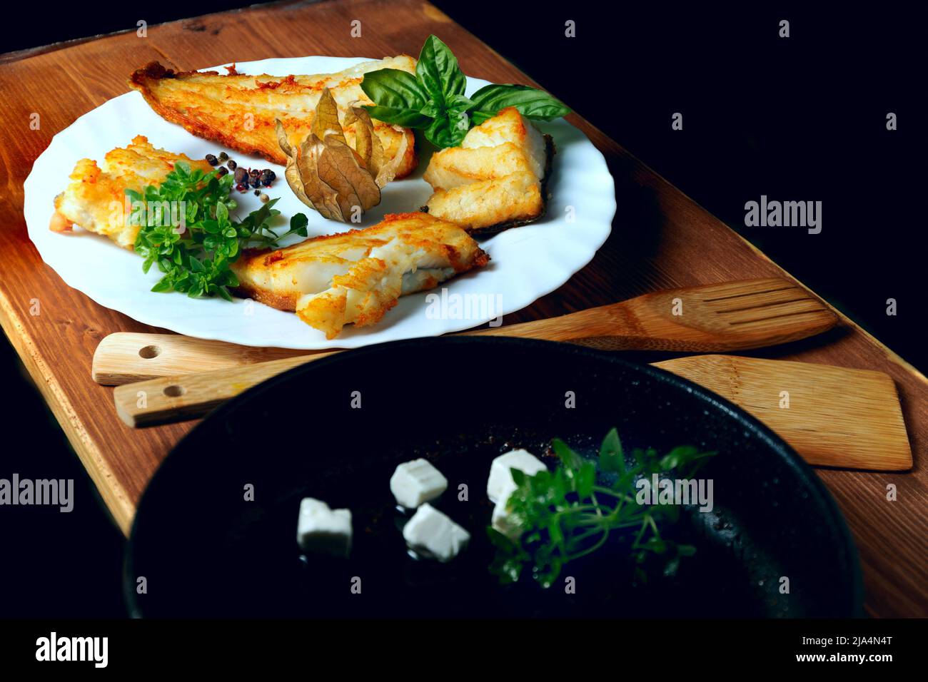 Filetti di merluzzo su un piatto bianco con finocchio ed erbe su un pannello di legno, Foto Stock
