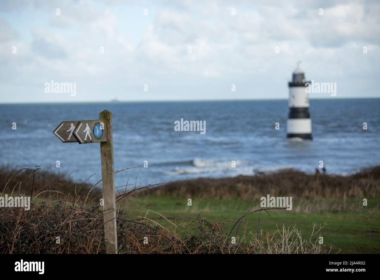 Cartello in legno della costa gallese con il faro di Trwyn du sullo sfondo Foto Stock