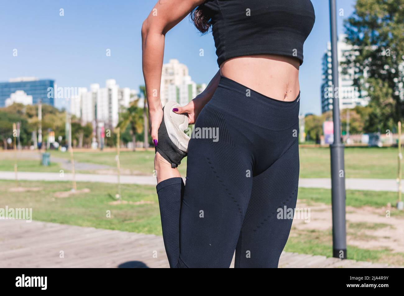 Giovane donna sportiva latinocaucasica irriconoscibile, con abbigliamento sportivo nero, muscoli esterni delle gambe stretching, routine sportiva mattutina. Foto Stock