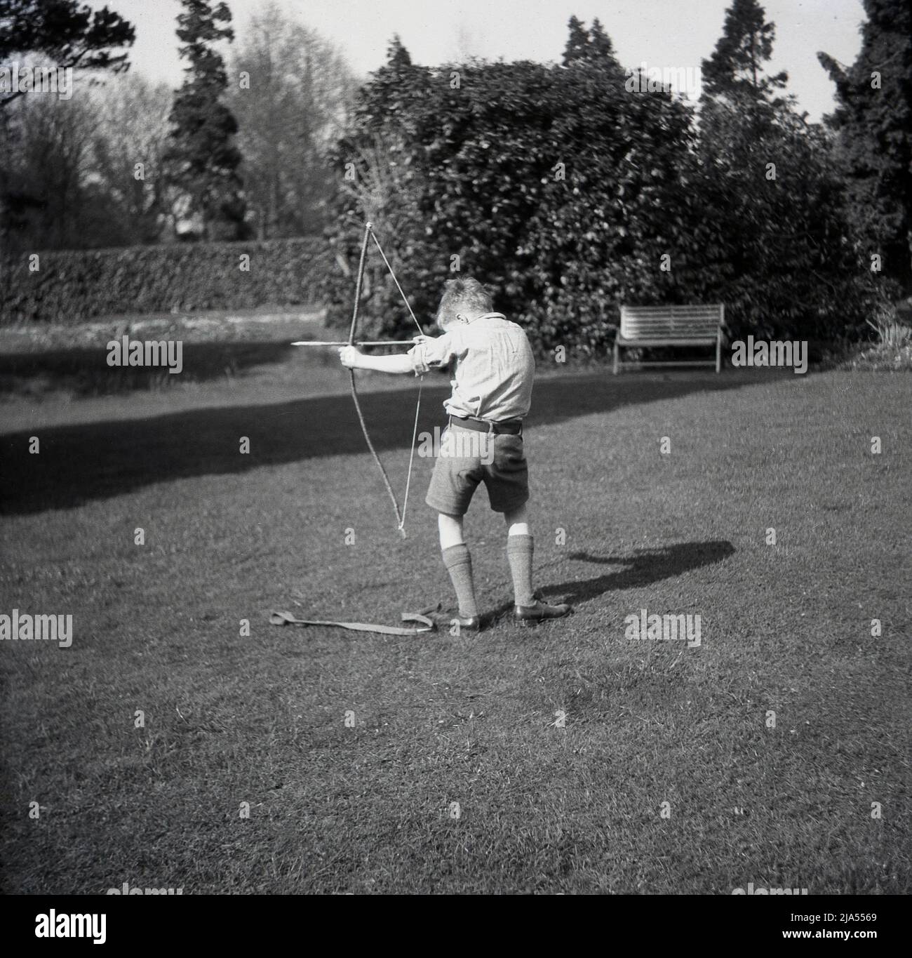 1950s, storico, fuori in un ampio giardino, un ragazzo con arco e freccia, prendendo AIM, Inghilterra, Regno Unito. Foto Stock