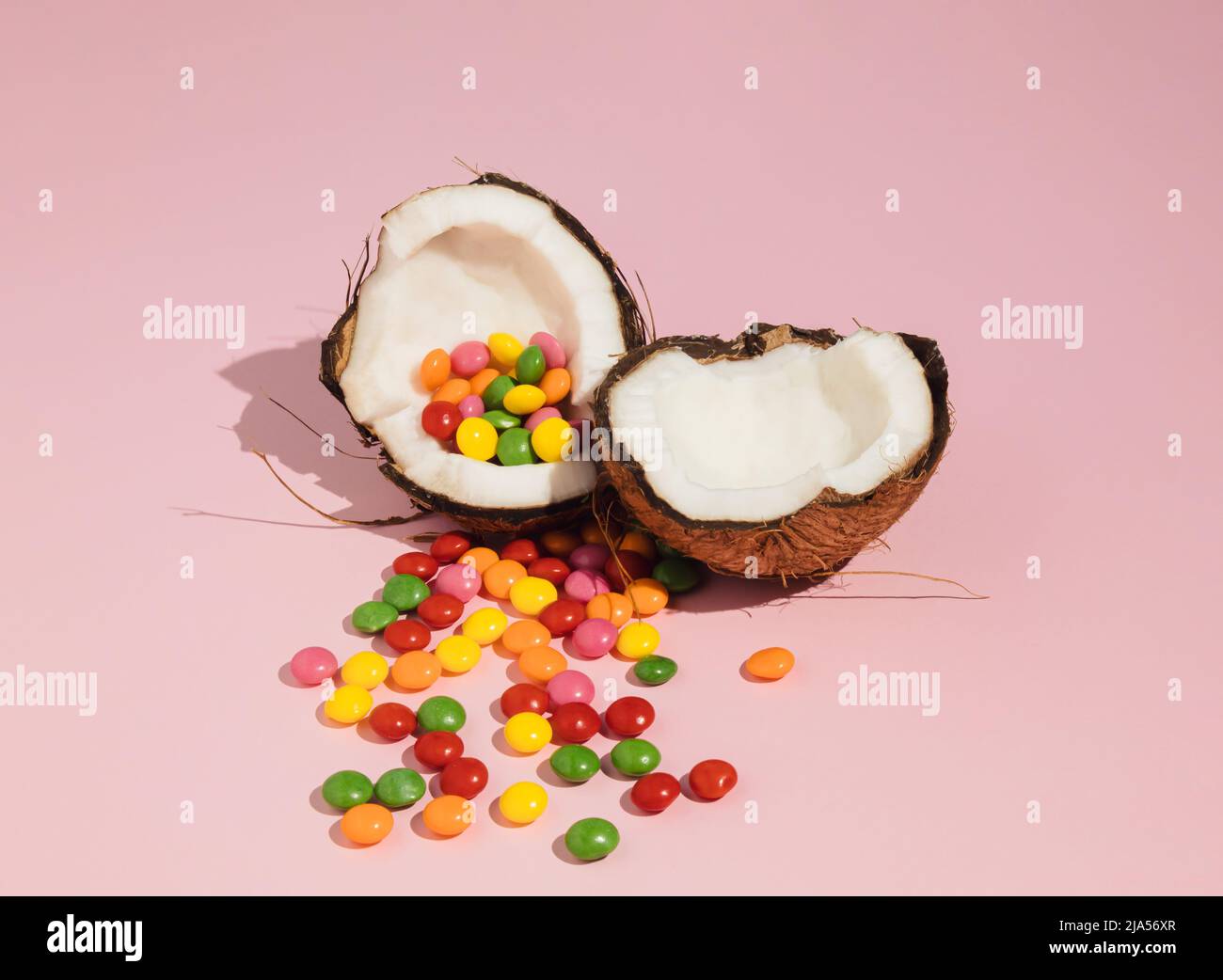 Cocco incrinato a metà e caramelle colorate. Un'idea estiva minima. Concetto di cibo creativo. Foto Stock