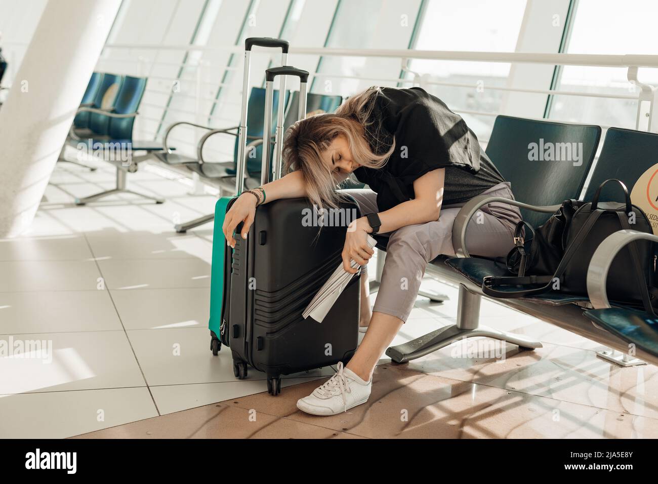 Passeggero stanco seduto su sedia in aeroporto moderno luce, sdraiato su valigie con abbigliamento e in attesa di arrivo aereo, ritardo del volo. Giovane Foto Stock