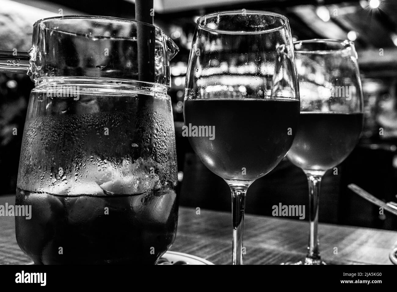 Una caraffa di sangria accompagnata da due bicchieri allineati su un tavolo di legno (bianco e nero). Foto Stock