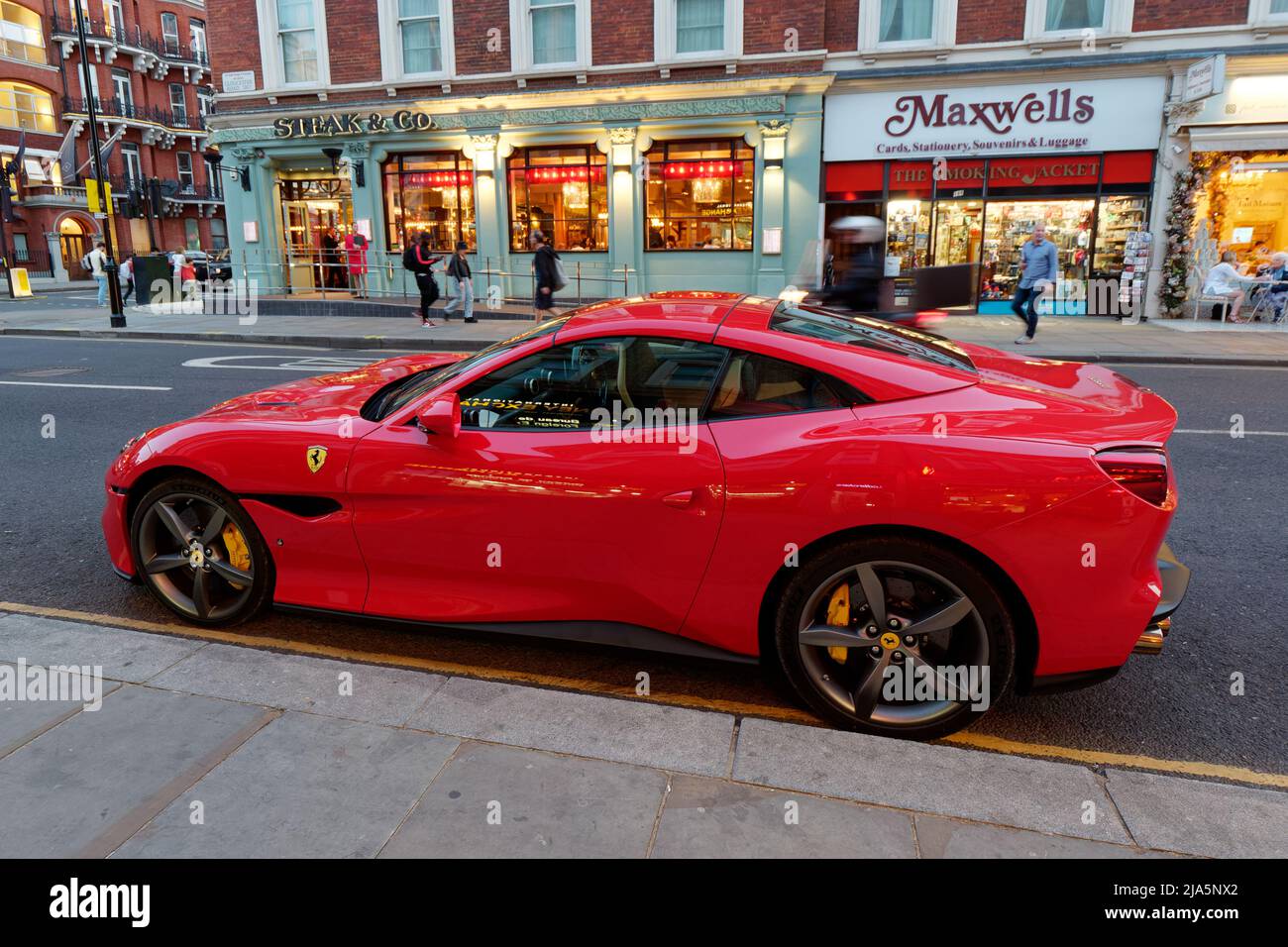 Londra, Greater London, Inghilterra, maggio 14 2022: Red Ferrari parcheggiata nei pressi di Gloucester Road di notte con il negozio e le luci del ristorante sulle spalle. Foto Stock