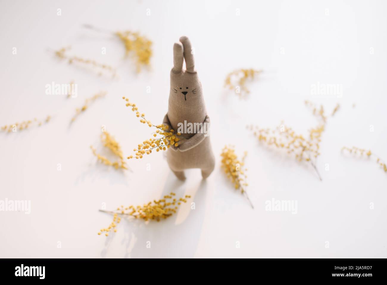 Divertente coniglio giocattolo fatto a mano che tiene fiori gialli. Concetto regalo di Pasqua. Foto Stock