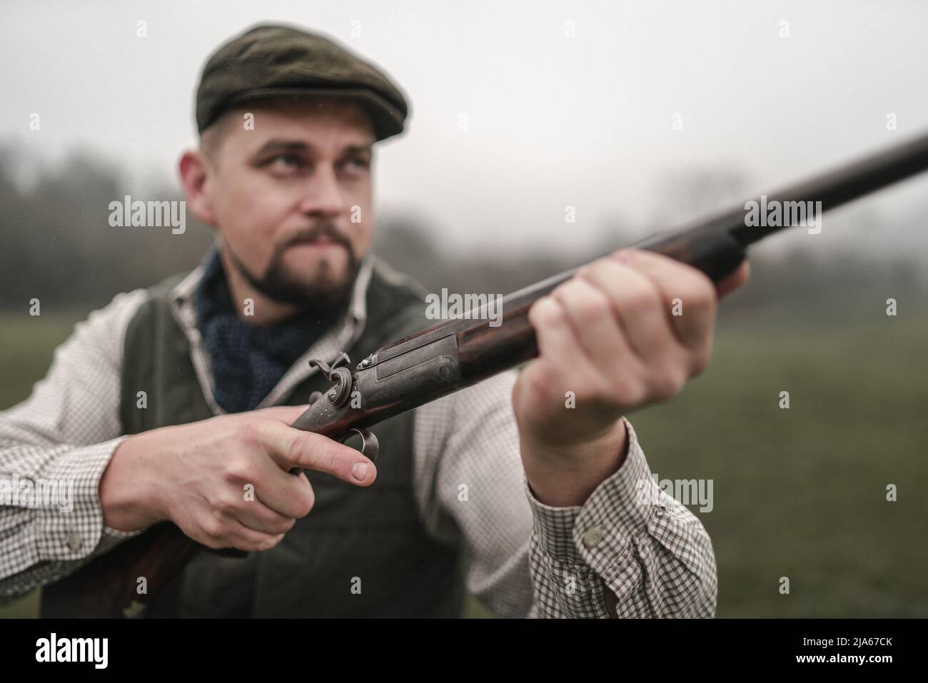 Hunter uomo in abiti da tiro tradizionali sul campo puntando con fucile. Foto Stock