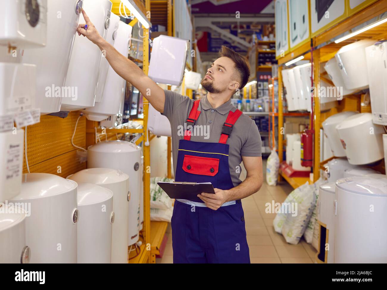 Addetto alle vendite con appunti che cammina lungo la corsia e controlla i riscaldatori elettrici dell'acqua Foto Stock