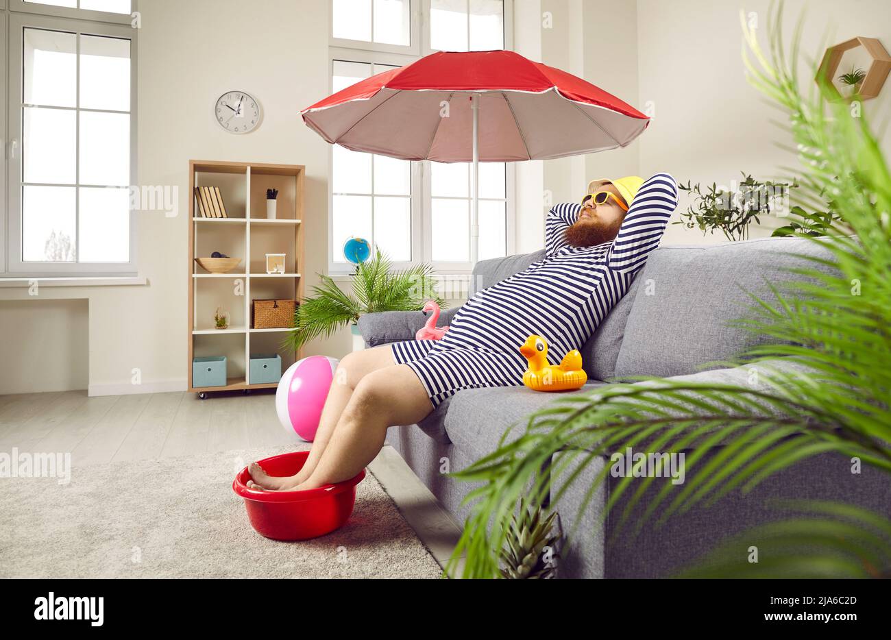 L'uomo divertente trascorre le vacanze estive a casa ma finge di rilassarsi sulla spiaggia Foto Stock