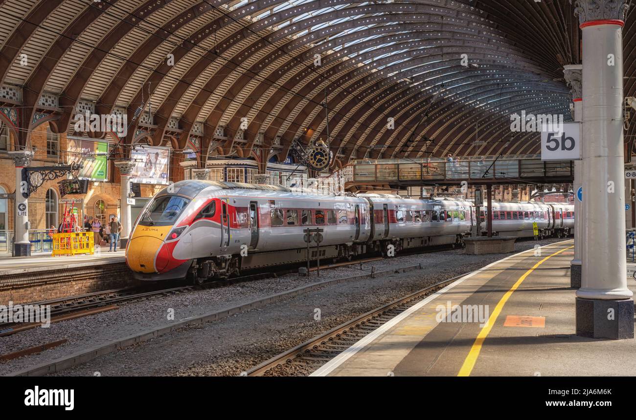 Un moderno treno si erge su una piattaforma storica con colonne e sotto un'ornata tettoia di ferro. Una passerella collega le piattaforme. Foto Stock