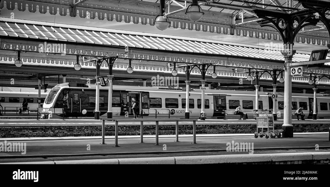 Una locomotiva si trova sotto le canopie storiche ornate. I passeggeri sono sulla piattaforma. Foto Stock