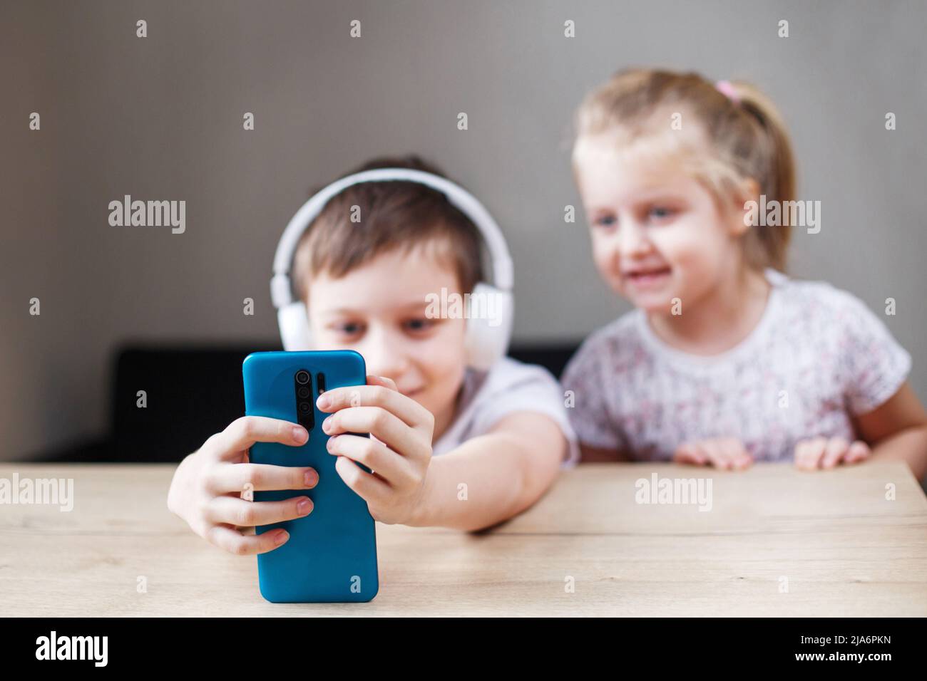due bambini che giocano sullo smartphone con le cuffie. persone, bambini e tecnologia concetto - bambini con il cellulare prendere selfie o avere videochiamata a Foto Stock