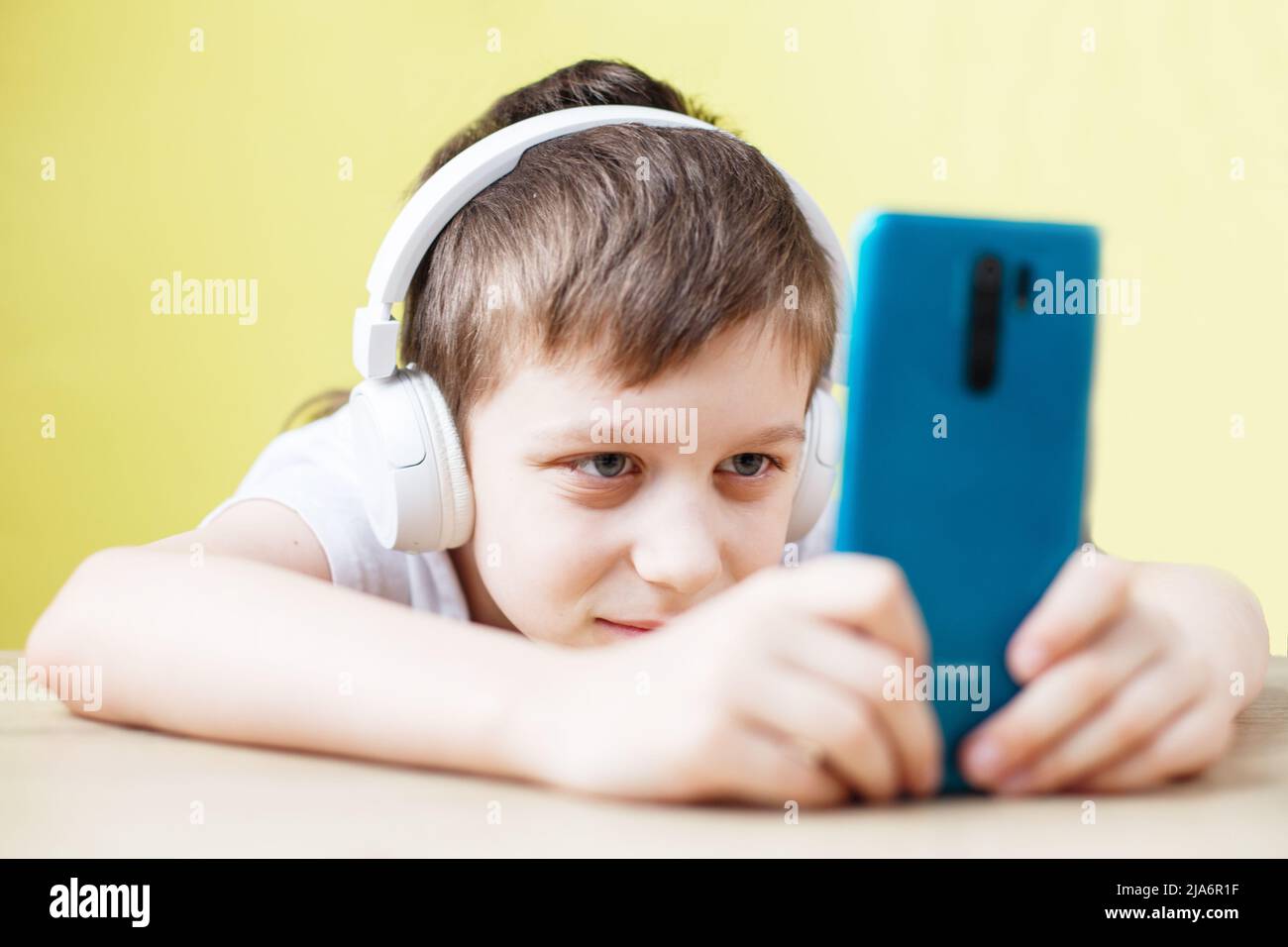 divertimento, bambini, tecnologia e concetto di gente - ragazzo sorridente con smartphone e cuffie che ha una videochiamata a casa. bambino con cellulare su un giallo Foto Stock