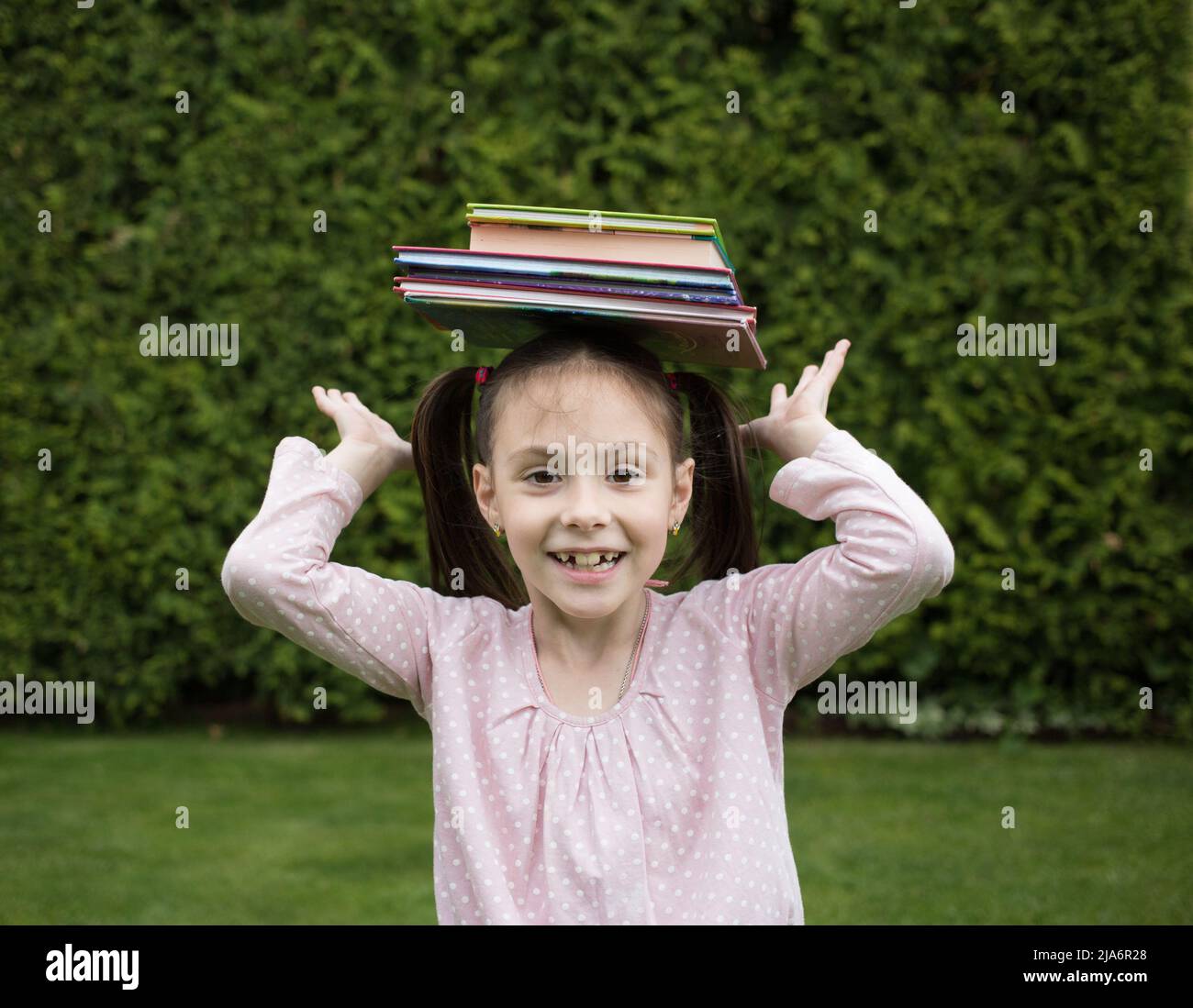 pila di libri sulla testa di una ragazza allegra di 7 anni. torna al concetto di scuola. L'estate è finita e la scuola inizia. Giorno della prenotazione. Leggi con piacere Foto Stock