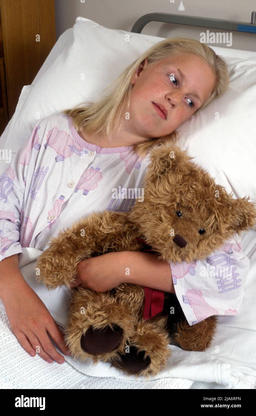 giovane ragazza in ospedale letto che si aggrappa orsacchiotto Foto Stock