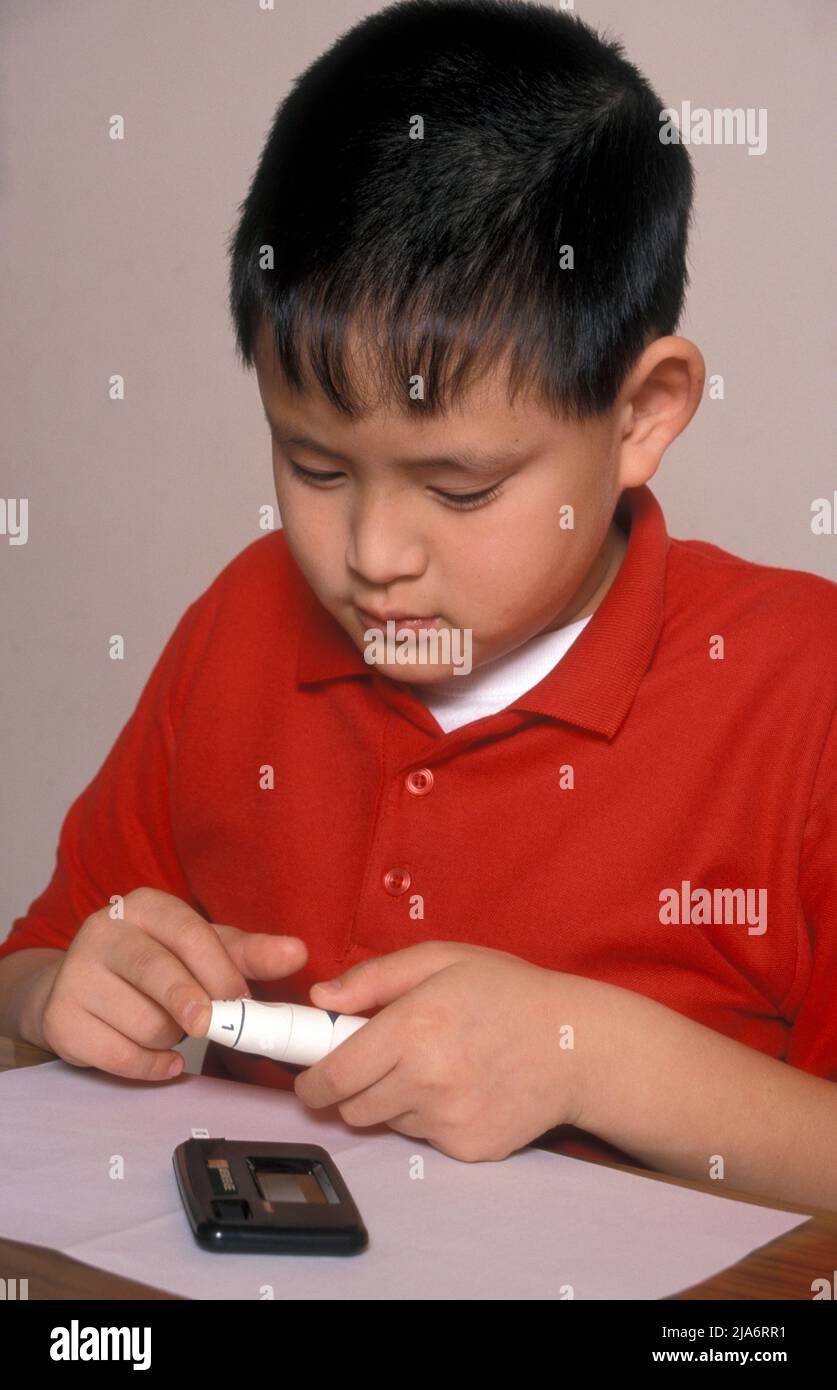 bambino orientale diabetico che fa il test del pulcino del dito per i livelli di glucosio Foto Stock