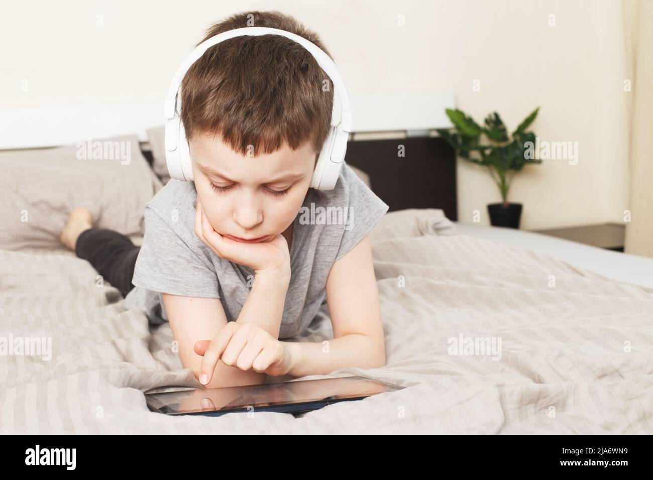 bambino che si trova a casa con un tablet pc e legge online, impara o ascolta musica con le cuffie wireless Foto Stock